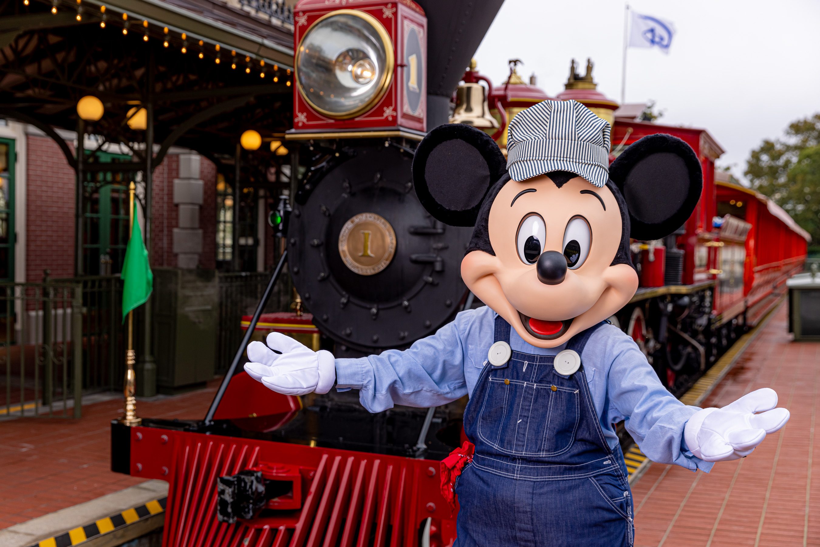 Mickey Mouse dressed as a train conductor in front of the park's railroad.