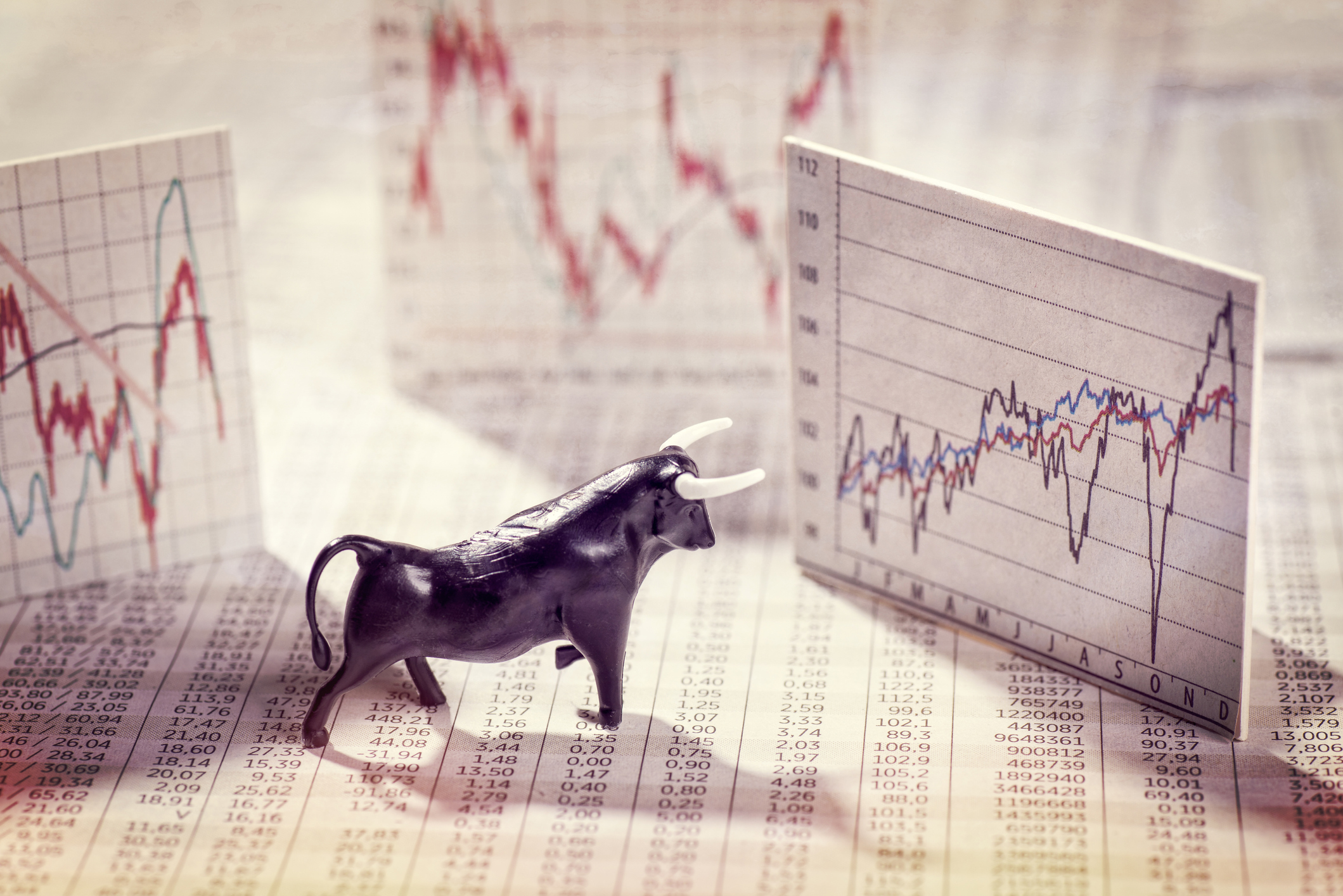 A bull figurine looking at a stock chart going up.