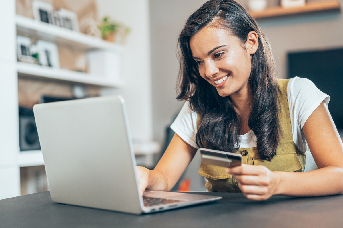 A smiling person with a credit card looks at a laptop. 