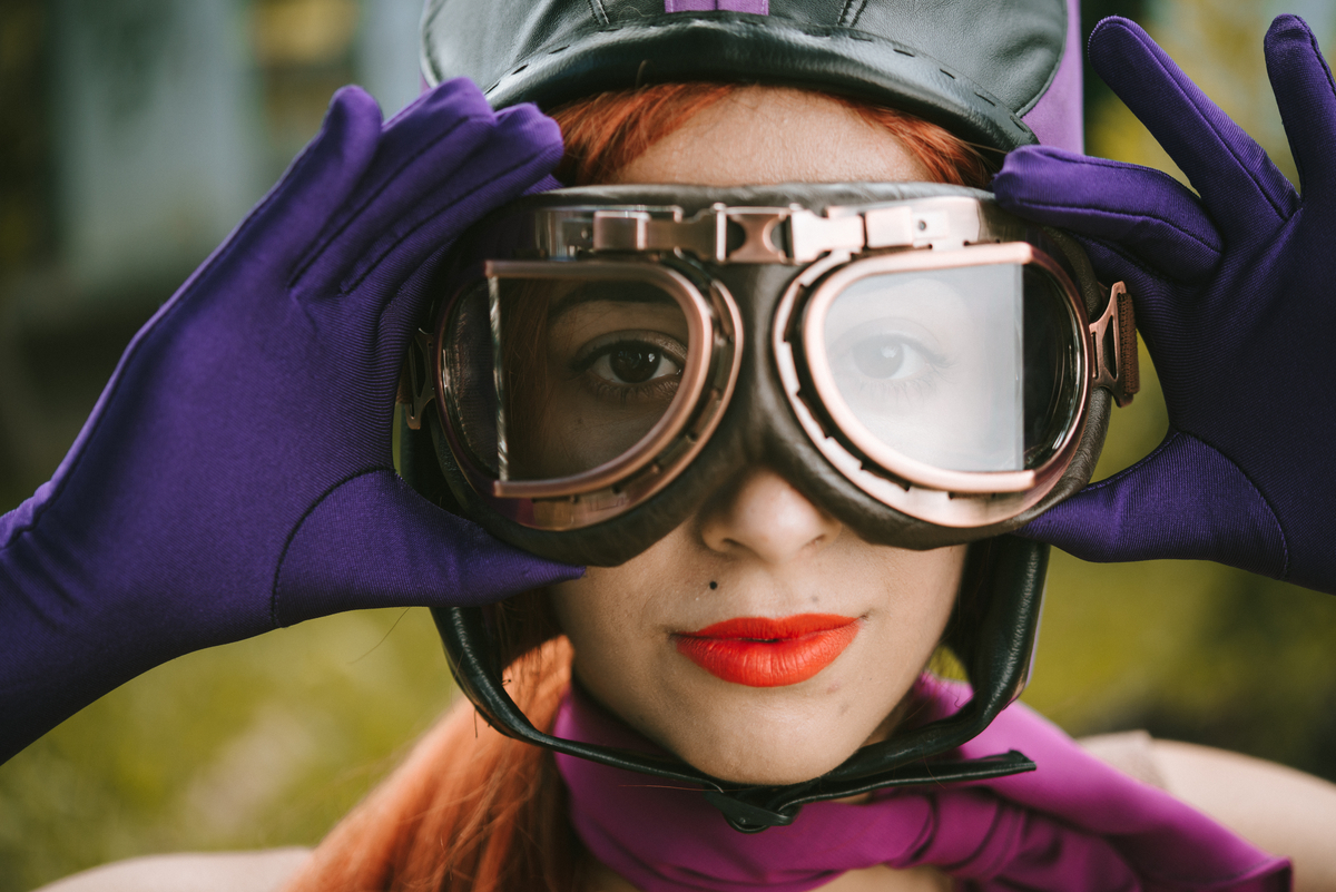 A person wearing aviator goggles and purple gloves.