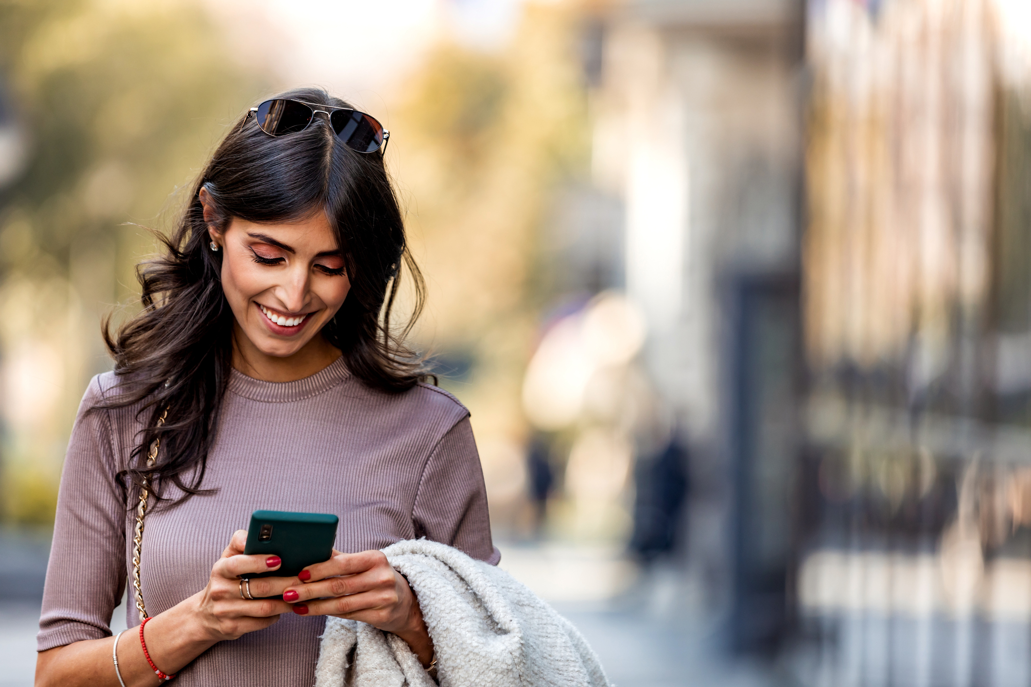 Person standing outside looking at a phone and smiling.