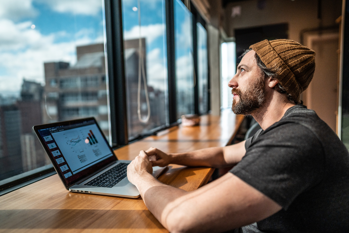 Person sitting in front of laptop is looking out office building windows.