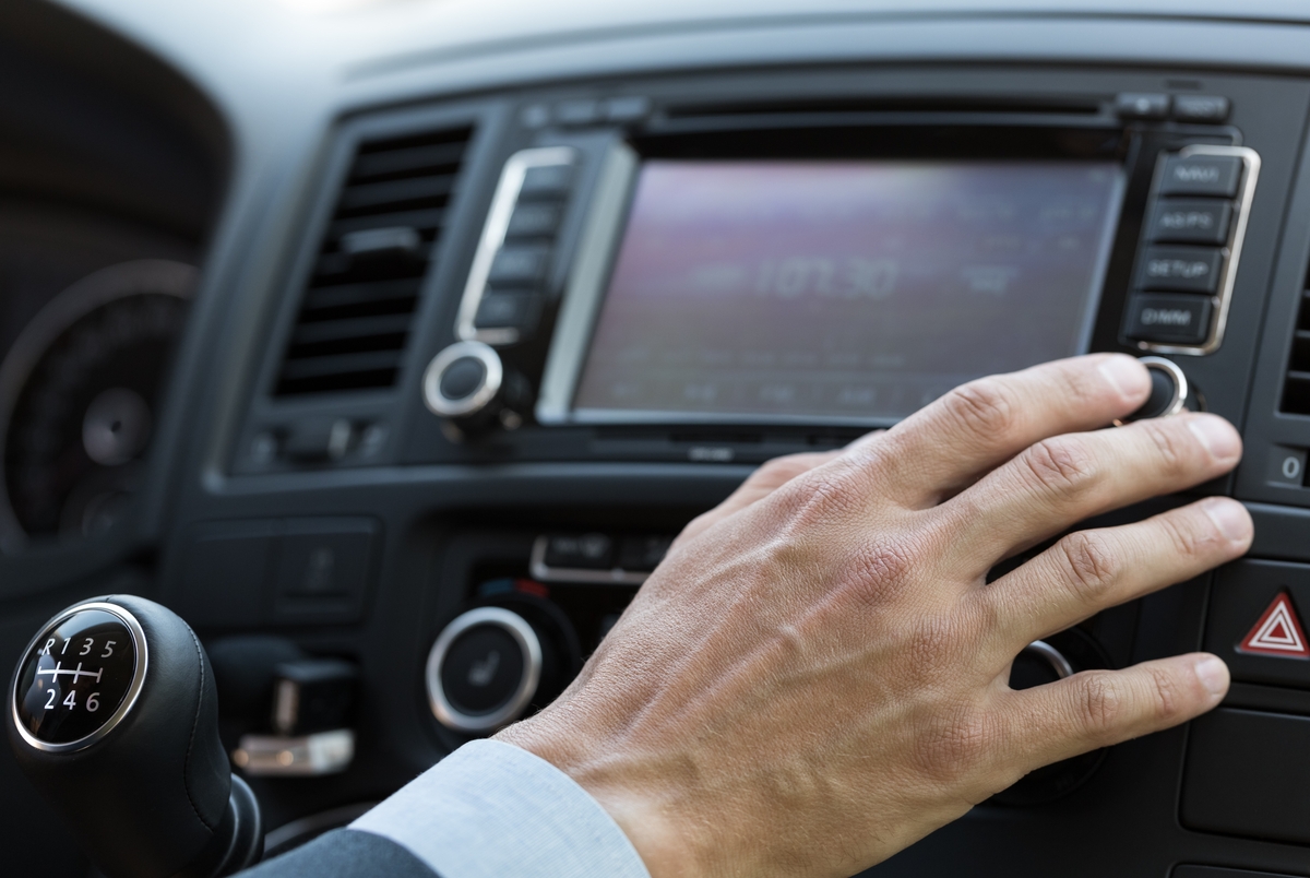 Human hand on the control panel of an automotive infotainment system.