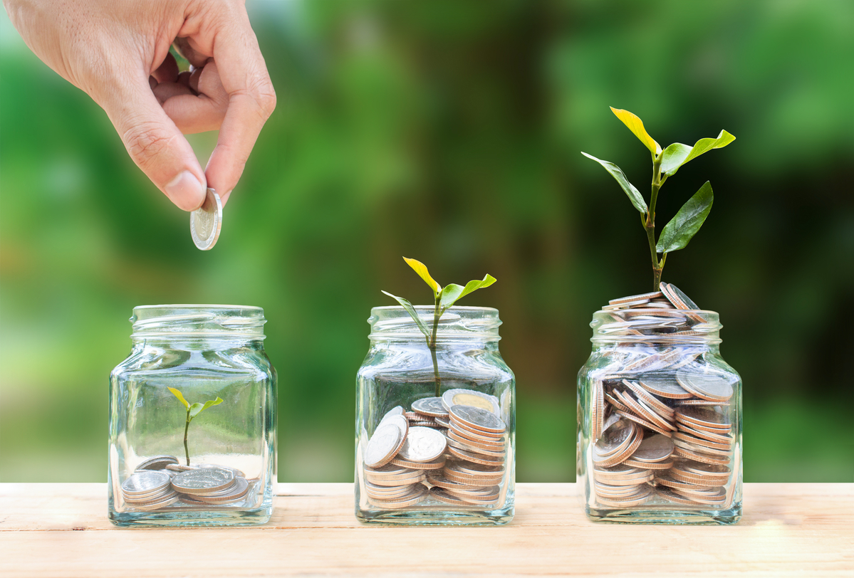 A person stacking coins into glass jars with plants sprouting from the jars, with the tallest plant emerging from the jar with the most coins. 