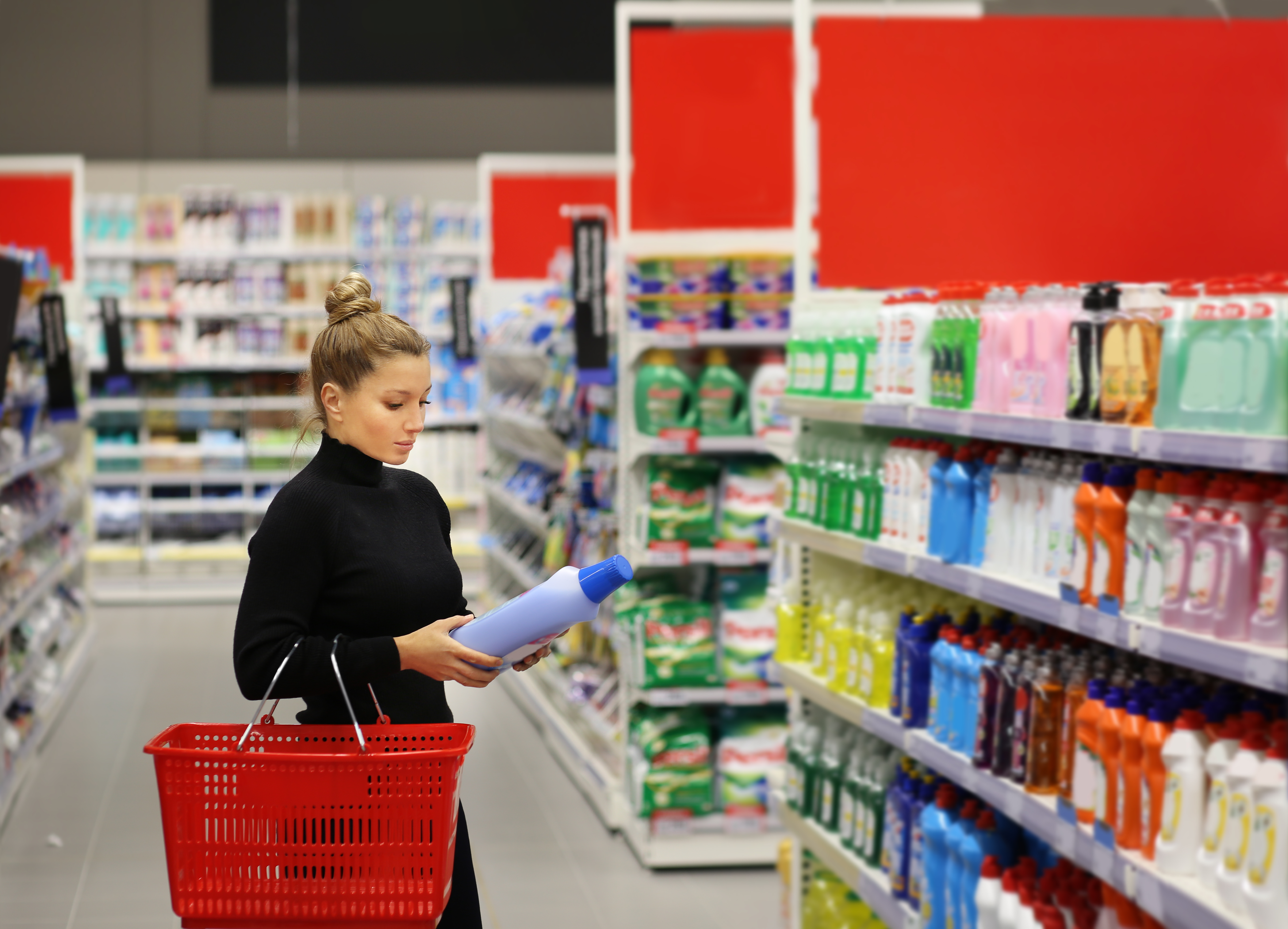 A shopper examining a large bottle of laundry detergent in the household-products section of a large store. 